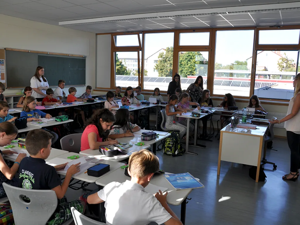 Blick in einen Klassenraum, in dem Kinder an ihren Plätzen arbeiten.
